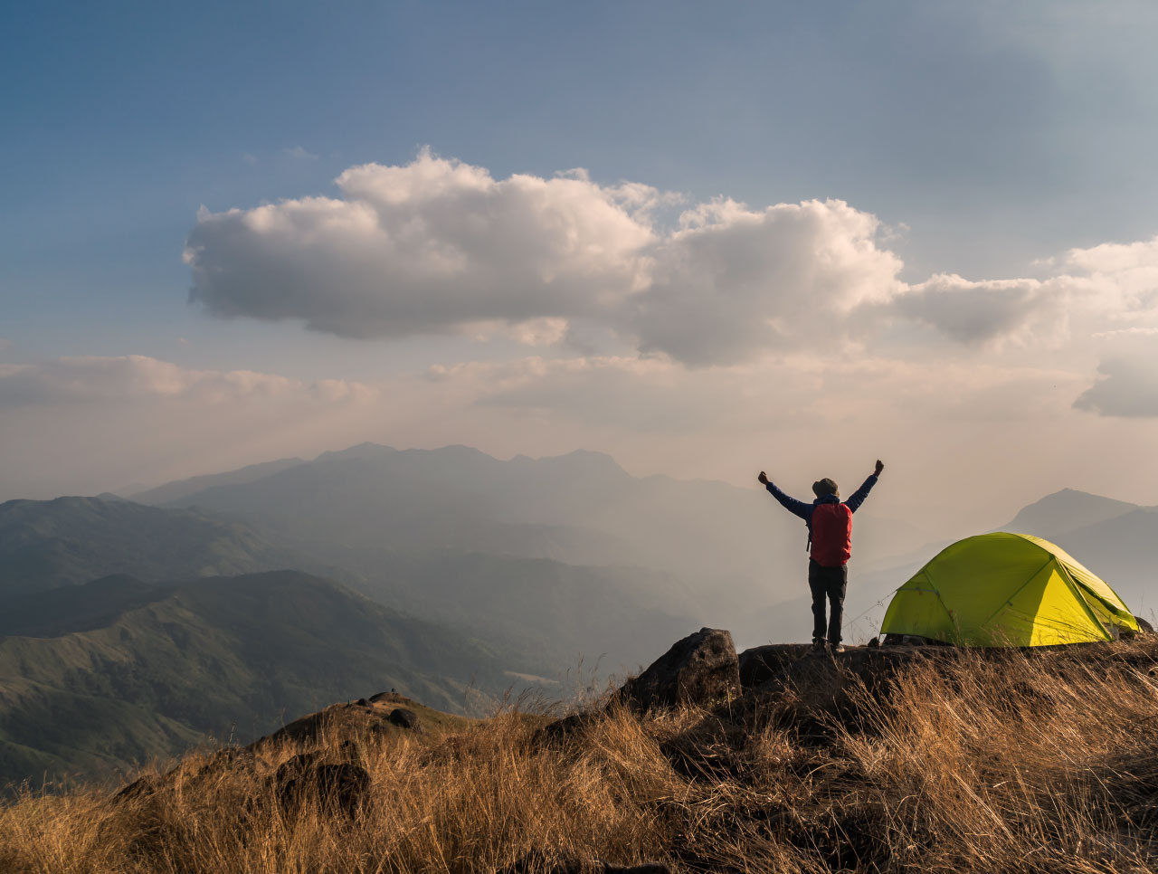 Hiker celebrating on a mountaintop beside a tent